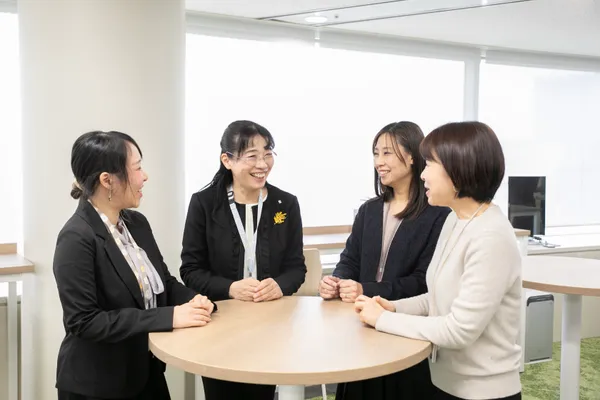 丸テーブルを囲んで立ちながら話をしている4名の女性。笑顔が見られる