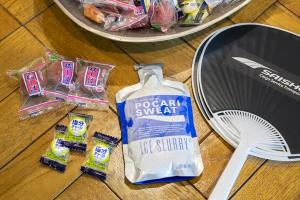 梅しば、塩分サポートタブレット、スポーツ飲料、うちわが机の上に並んでいる